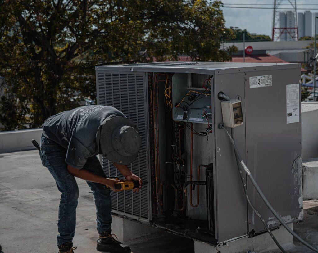 HVAC technician in work boots drilling an outdoor air conditioning condenser unit on a rooftop
