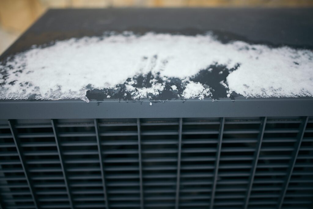 Snow-covered outdoor air conditioning condenser unit in a residential area during winter weather